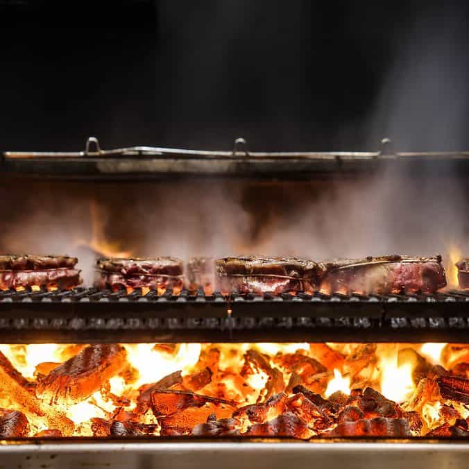 Barbecue grilling with flames and sizzling meat on a grill.