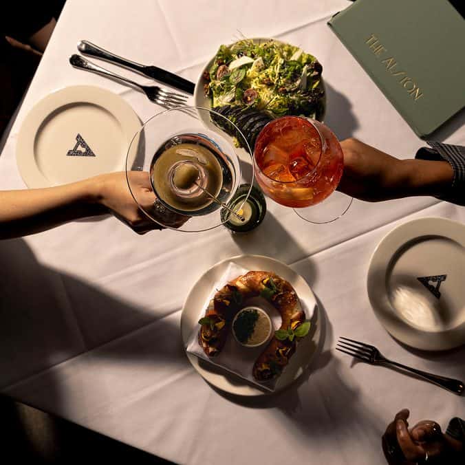 Two people touching drink glasses, sitting at a table with a salad and bread.
