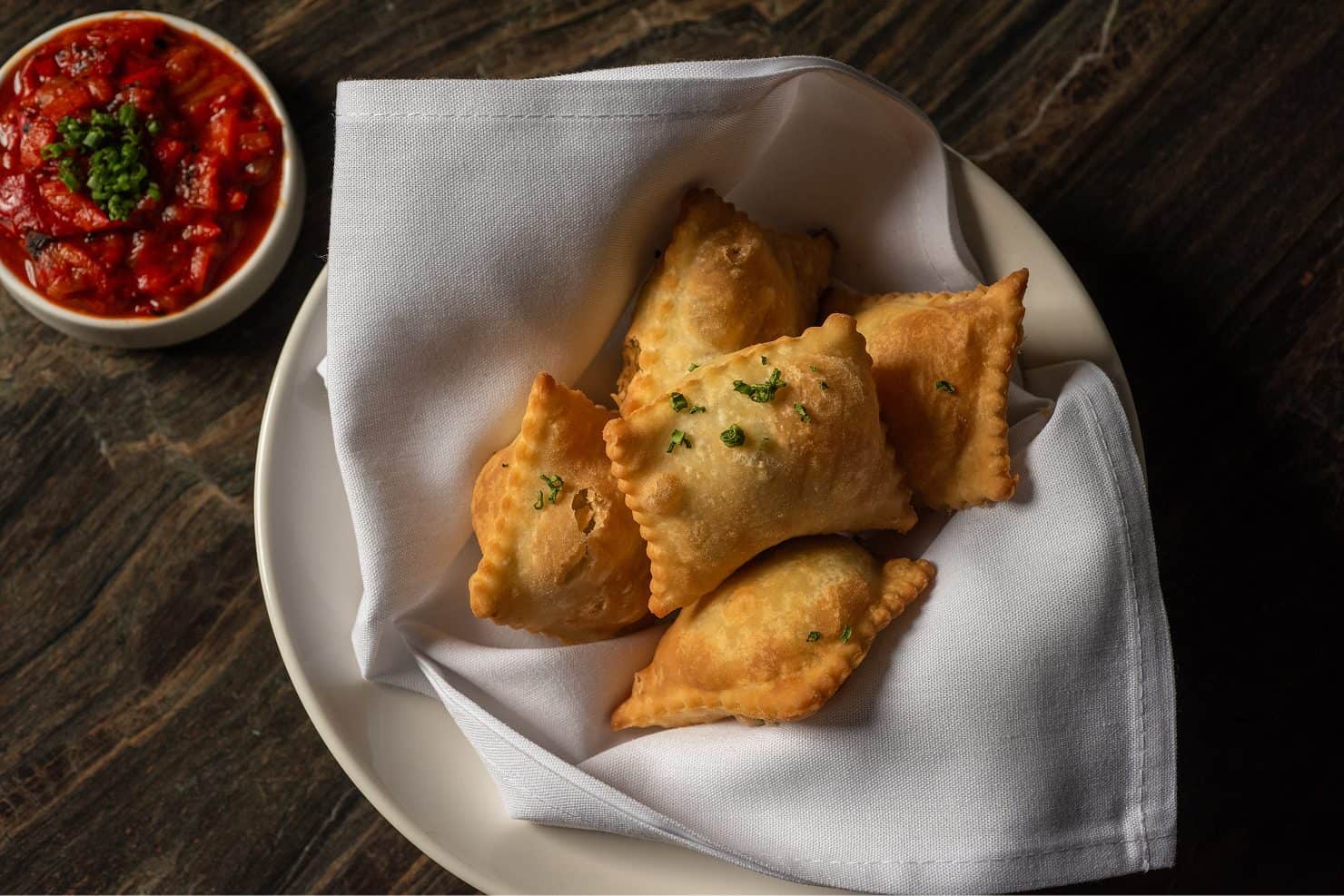 Fried empanadas served with a side of salsa in a white bowl.
