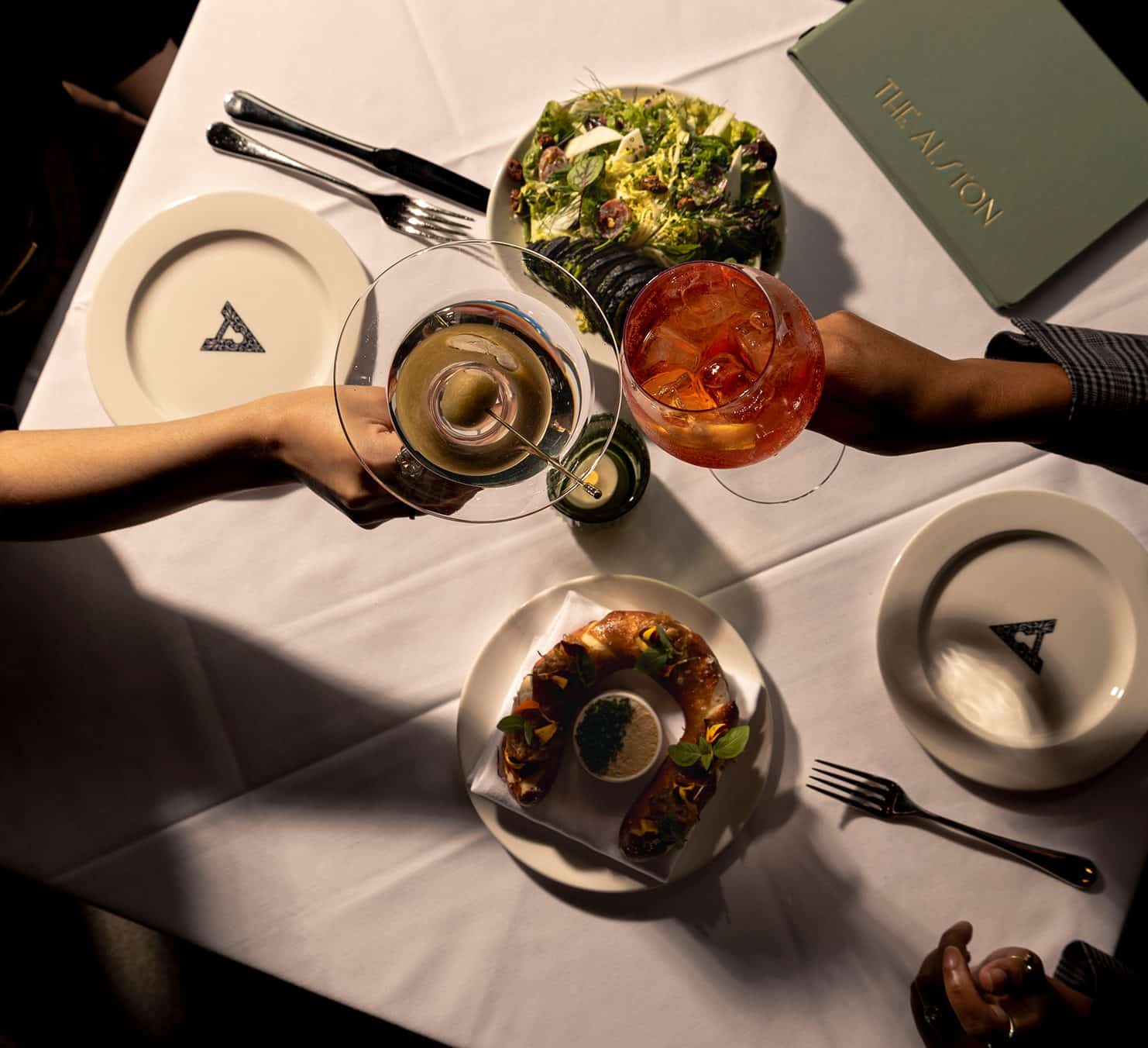 Elegant dining scene with salads, drinks, and tableware at The Alston restaurant.