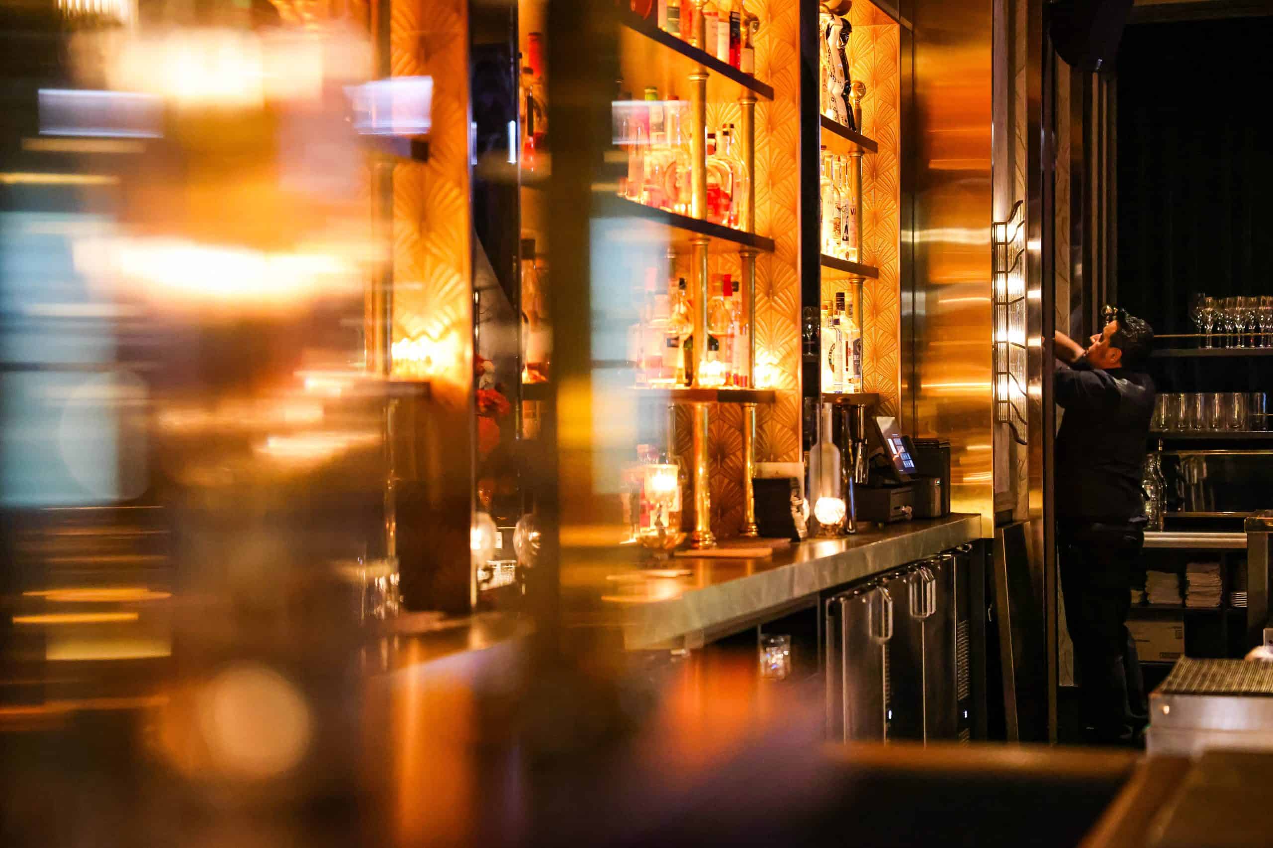 Bar interior with illuminated shelves and bartender serving drinks.