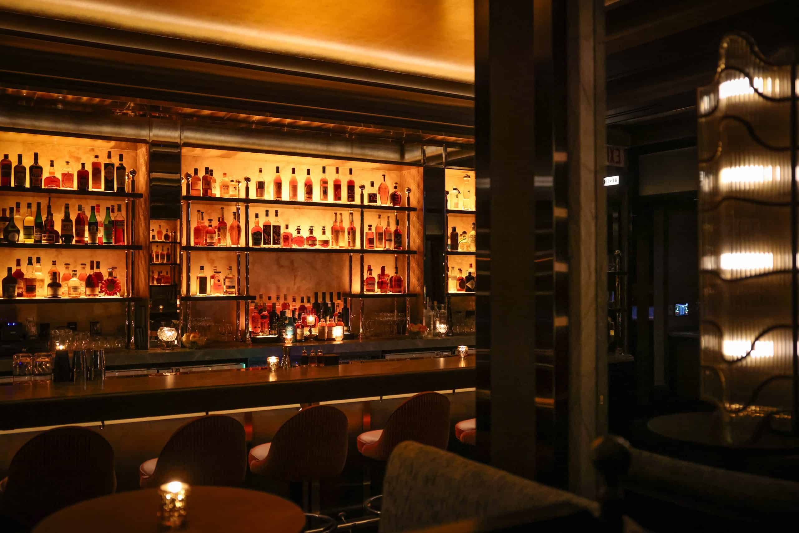 Stylish bar with illuminated shelves and cozy seating at The Alston.