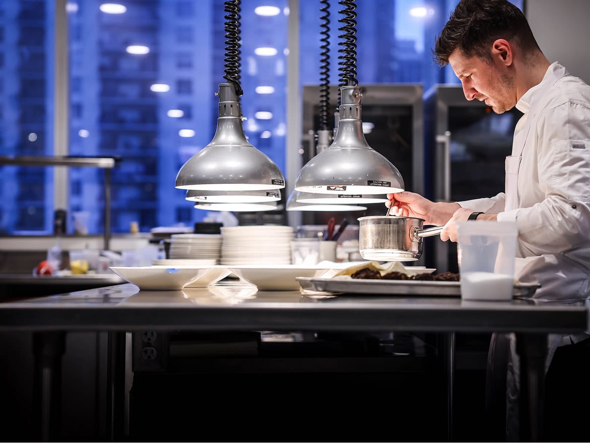 Chef preparing a dish in a modern kitchen at The Alston Members Club.