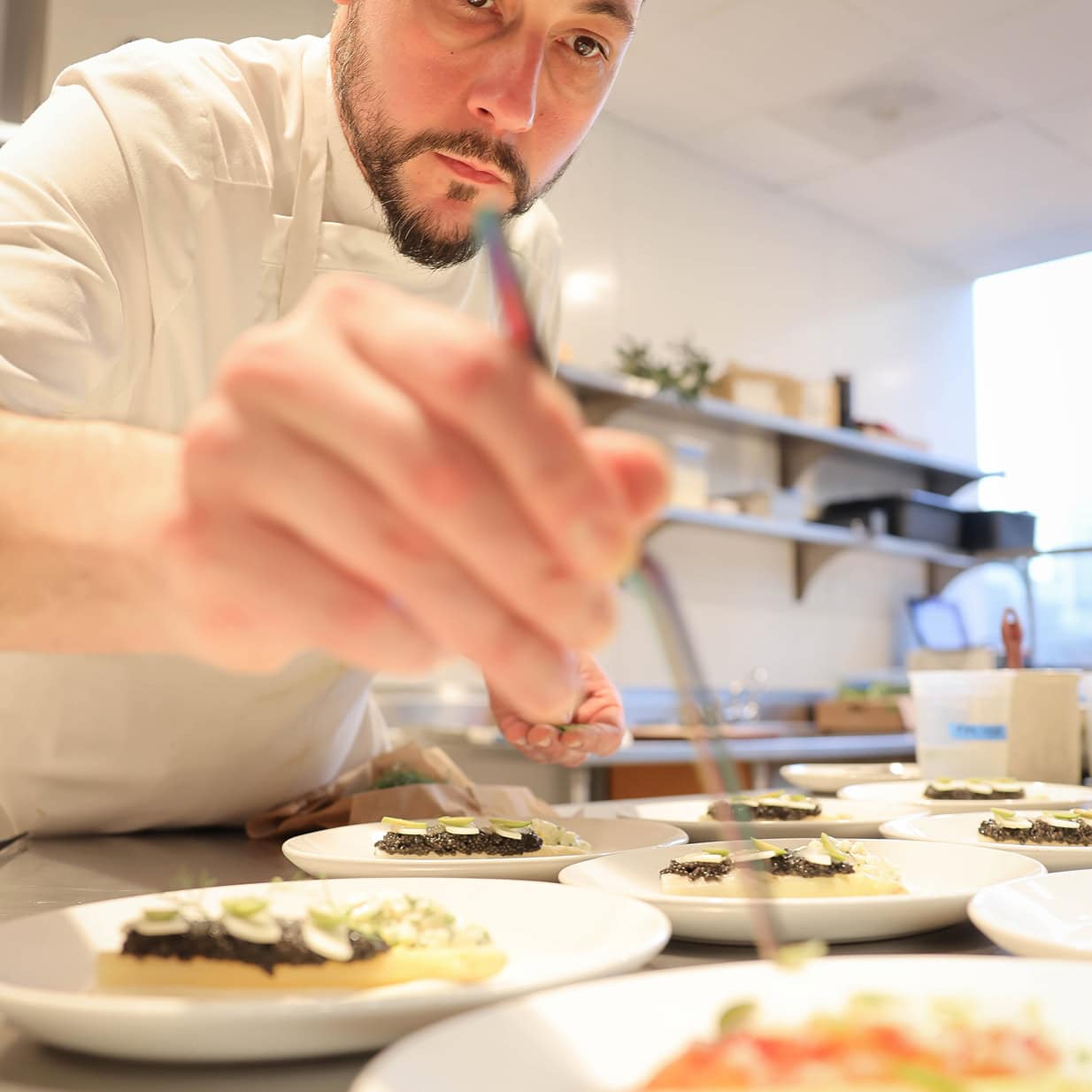 Chef garnishing gourmet dishes in a modern kitchen at The Alston.