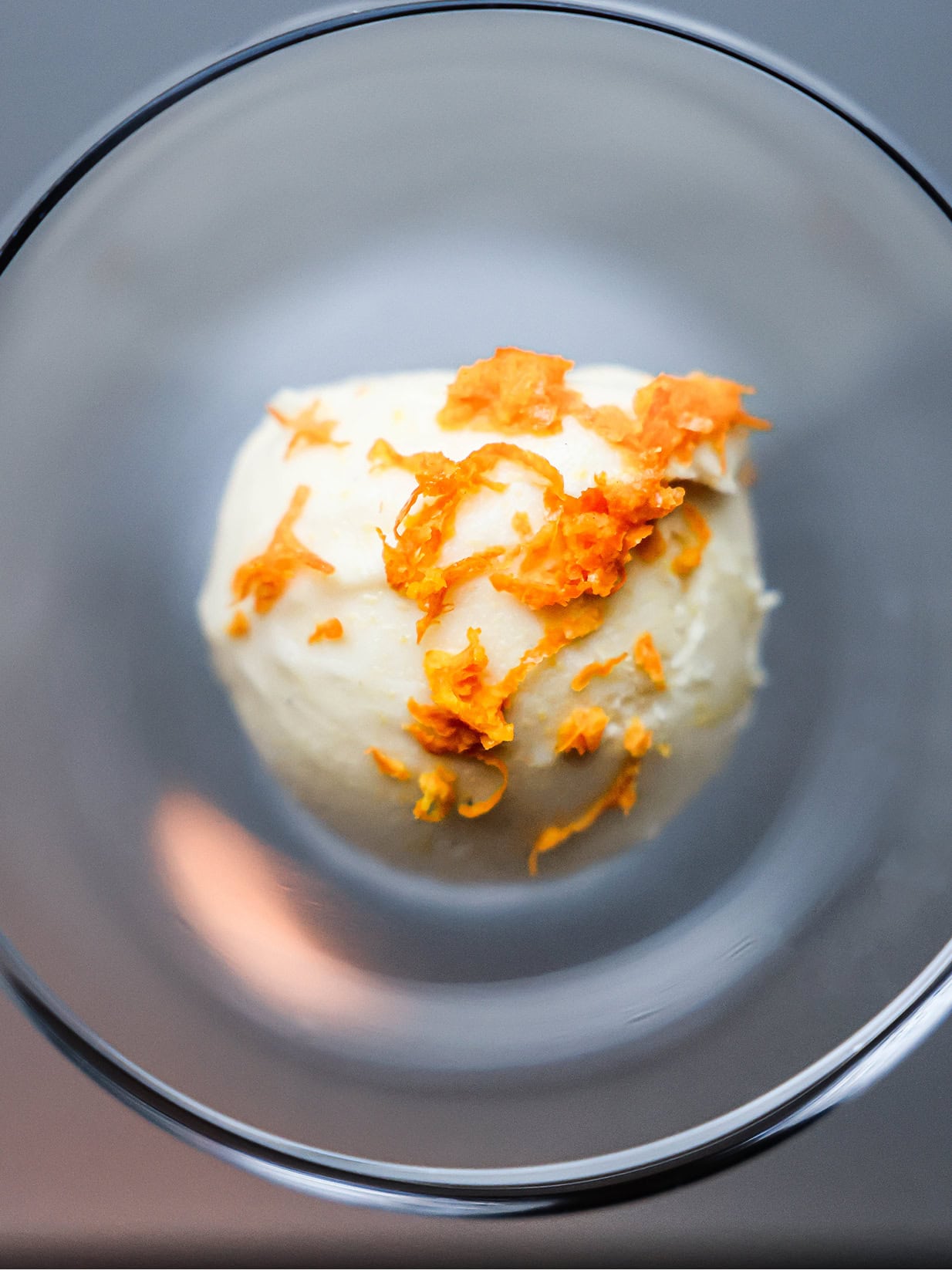 Creamy dessert topped with orange zest in a glass bowl.